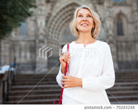 Cheerful mature female is walking in white blouse on the street outdoor Cheerful mature female is walking in white blouse on the street outdoor 70283288