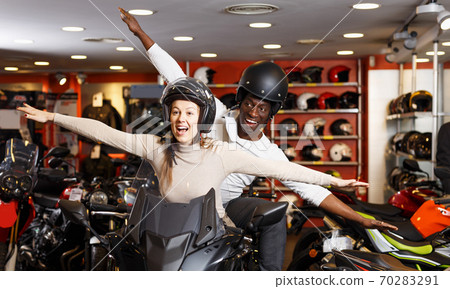 Couple sitting together on new motorcycle in store and having fun Couple sitting together on new motorcycle in store and having fun 70283291