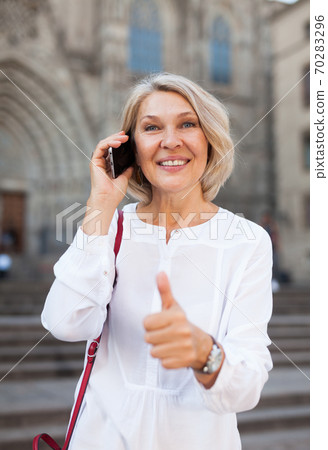 Happy woman talking on smartphone and holds thumb up 70283296