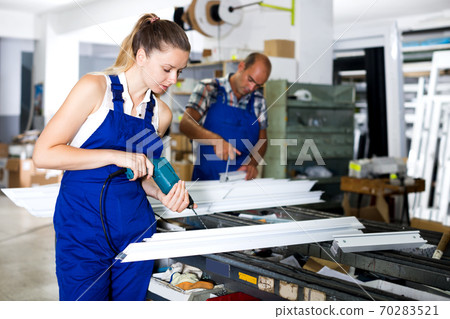 Workwoman drilling PVC window profiles in workshop 70283521