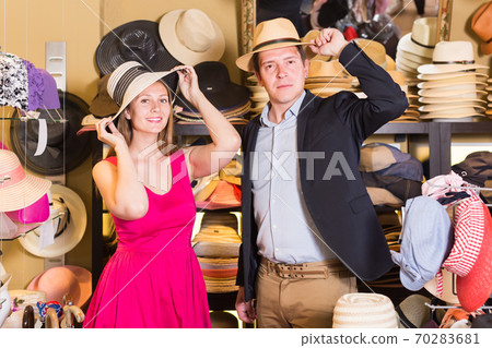 cheerful young female and man choosing hats in the store cheerful young female and man choosing hats in the store 70283681