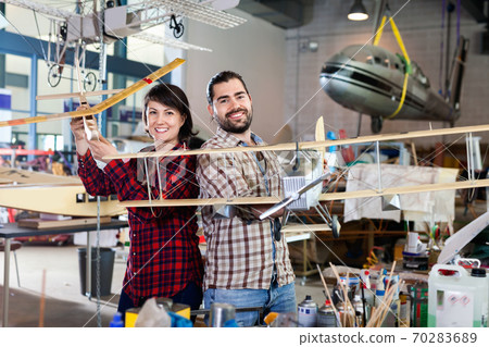 Cheerful team of aircraft enthusiasts holding sports airplane models in workshop Cheerful team of aircraft enthusiasts holding sports airplane models in workshop 70283689