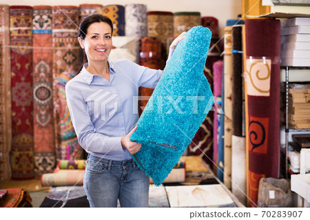 Smiling woman customer holding colorful carpet Smiling woman customer holding colorful carpet 70283907