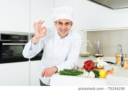 Male cook in white uniform showing ok hand sign on kitchen 70284290