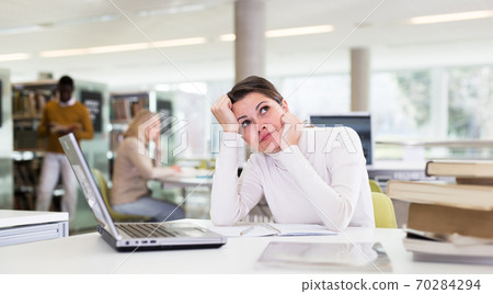 Portrait of upset tired female student preparing for exam in university library 70284294