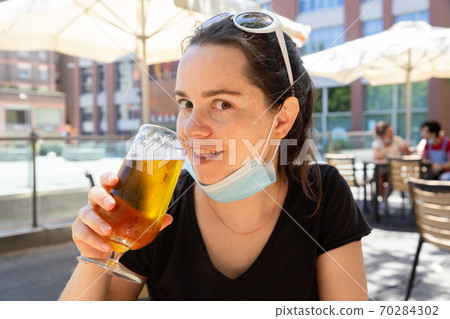 Woman in surgical mask with beer on open bar terrace Woman in surgical mask with beer on open bar terrace 70284302