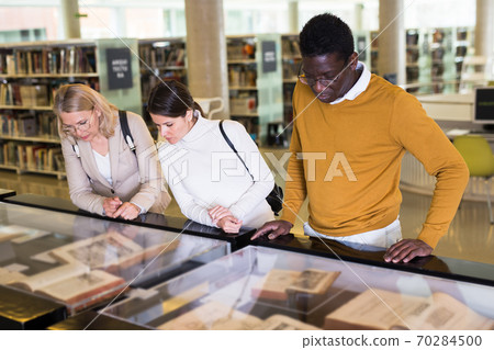 Teacher and adult students view rare books in a library showcase 70284500