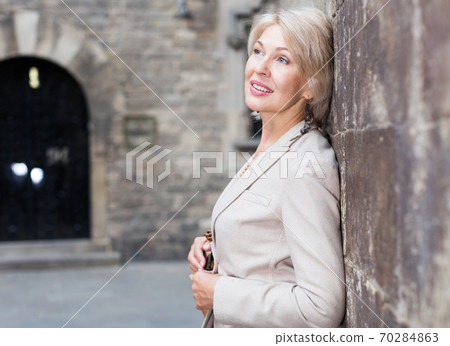Cheerful mature female is playfully posing near wall 70284863