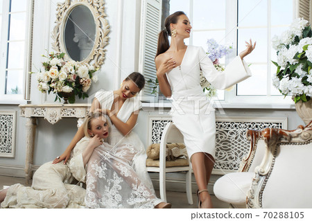 three young pretty lady in white lace fashion style dress posing in rich interior of royal hotel room, luxury lifestyle people concept, bride on wedding day 70288105