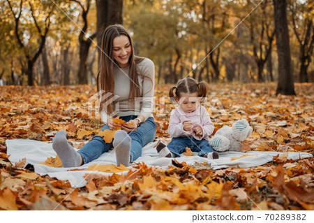 Happy family mom and toddler baby girl playing outdoors in fall park. Little girl and her mother in the autumn park Happy family mom and toddler baby girl playing outdoors in fall park. Little girl and her mother in the autumn park 70289382