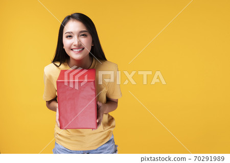 Friendly young woman holding red gift box in her hands while looking at camera over isolated Friendly young woman holding red gift box in her hands while looking at camera over isolated 70291989