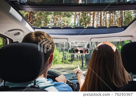 Couple in the car travelling on the road through trees. Couple in the car travelling on the road through trees. 70293367
