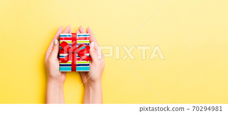 Woman arms holding gift box with colored ribbon on yellow table background, top view and copy space for you design 70294981