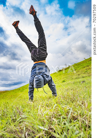 teenager stands on his hands upside down on the grass teenager stands on his hands upside down on the grass 70297509