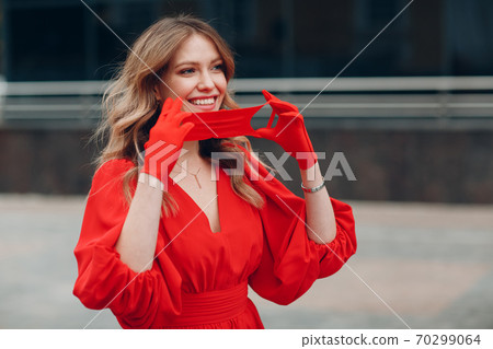 Young woman in red dress and gloves put on medical potective face mask 70299064