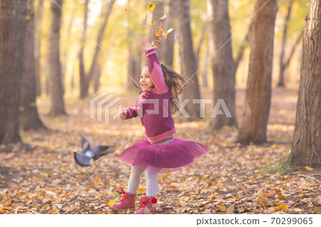 Cute little girl in autumn park with orange and yellow color leaves and flying bird 70299065