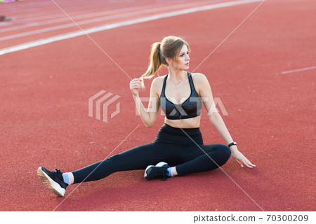 A female coach with dark hair stands on the red running track of the stadium A female coach with dark hair stands on the red running track of the stadium 70300209