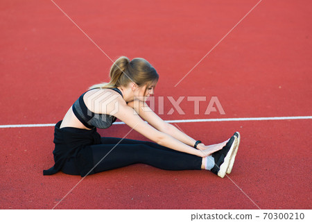 A female coach with dark hair stands on the red running track of the stadium A female coach with dark hair stands on the red running track of the stadium 70300210