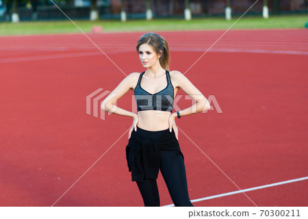 A female coach with dark hair stands on the red running track of the stadium A female coach with dark hair stands on the red running track of the stadium 70300211