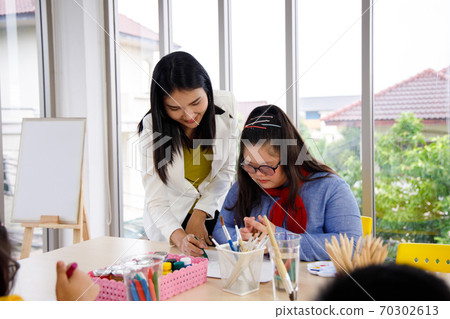 Teacher teaches art to girl with Down's syndrome in classroom. Concept disabled kid learning. 70302613