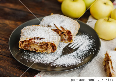 Apple strudel with icing sugar and raisins on black plate 70306155