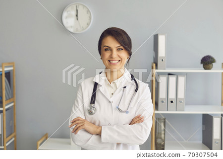 Smiling woman doctor therapist sitting in medical clinic office and looking at camera Smiling woman doctor therapist sitting in medical clinic office and looking at camera 70307504