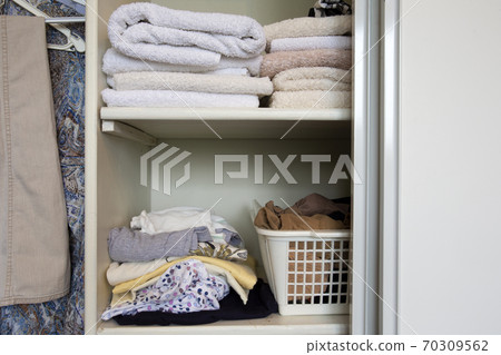 Full closet with clothes and Stack of towels in white wooden closet, organization and storage Full closet with clothes and Stack of towels in white wooden closet, organization and storage 70309562