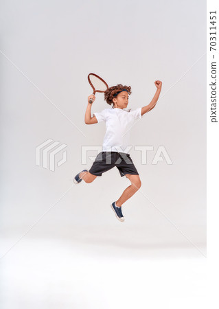 Little winner. Full-length shot of a teenage boy jumping with a tennis racket isolated over grey background, studio shot. Little winner. Full-length shot of a teenage boy jumping with a tennis racket isolated over grey background, studio shot. 70311451
