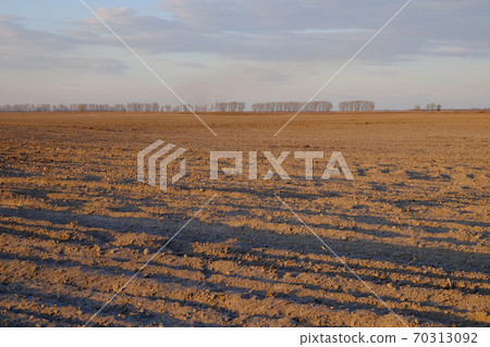 Cloudy evening sky over an empty agricultural field. Bright sunset landscape. 70313092
