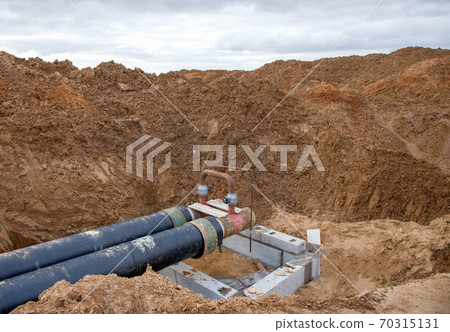 Laying heating pipes in a trench at construction site. 70315131