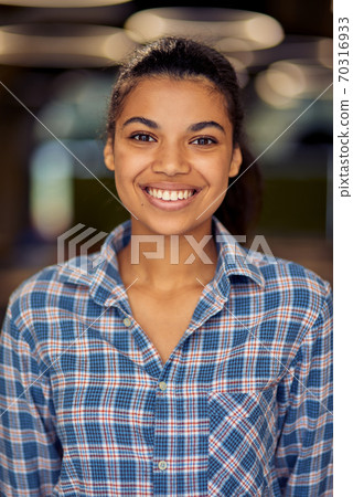 Vertical shot of a young happy mixed race business woman in casual wear looking at camera and smiling while posing in the office Vertical shot of a young happy mixed race business woman in casual wear looking at camera and smiling while posing in the office 70316933