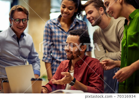 Group of happy multiracial business people looking at laptop screen and discussing work or project results while standing in the modern office or coworking space Group of happy multiracial business people looking at laptop screen and discussing work or project results while standing in the modern office or coworking space 70316934