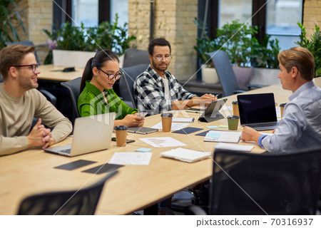 Group of young multiracial business people sitting at desk in the board room and working on project together, discussing work and sharing ideas Group of young multiracial business people sitting at desk in the board room and working on project together, discussing work and sharing ideas 70316937