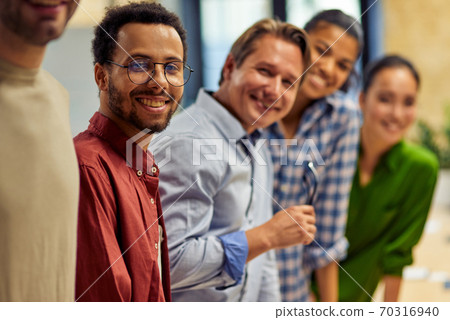 Successful team. Group of young happy multi ethnic business team looking at camera and smiling while standing in the modern office, working together Successful team. Group of young happy multi ethnic business team looking at camera and smiling while standing in the modern office, working together 70316940