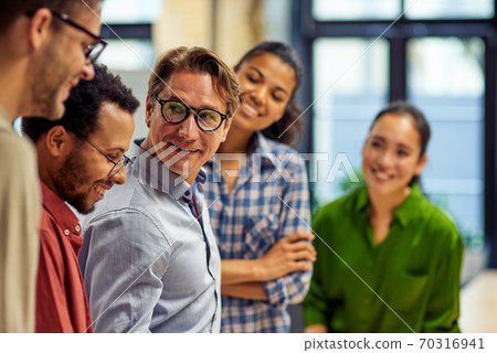 Confident businessman discussing project results and sharing ideas with young motivated multi ethnic team while standing together in the modern office Confident businessman discussing project results and sharing ideas with young motivated multi ethnic team while standing together in the modern office 70316941