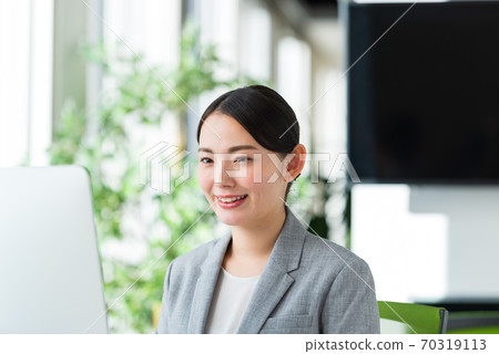 A young business woman operating a computer by the window of a bright office 70319113