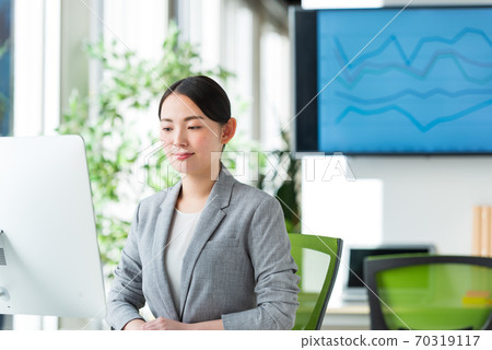 A young business woman operating a computer by the window of a bright office 70319117