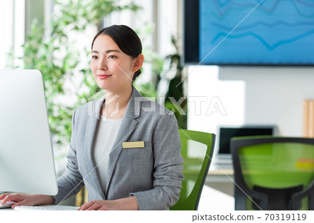 A young business woman operating a computer by the window of a bright office 70319119