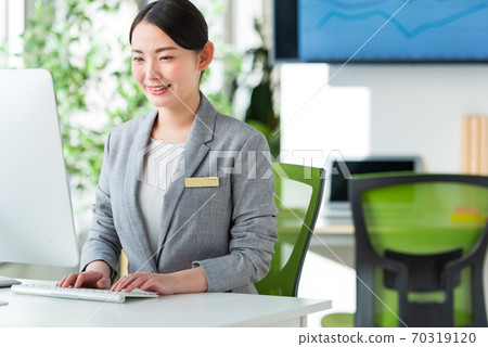 A young business woman operating a computer by the window of a bright office 70319120