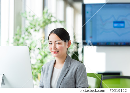 A young business woman operating a computer by the window of a bright office 70319122