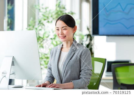 A young business woman operating a computer by the window of a bright office 70319125
