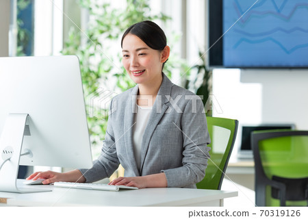 A young business woman operating a computer by the window of a bright office 70319126