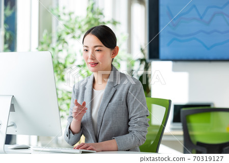 A young business woman operating a computer by the window of a bright office 70319127