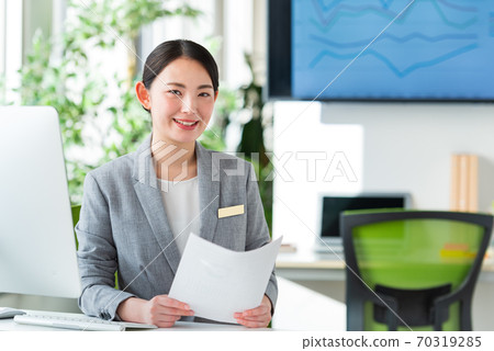 A young business woman operating a computer by the window of a bright office 70319285