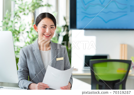 A young business woman operating a computer by the window of a bright office 70319287