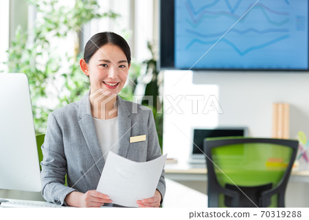 A young business woman operating a computer by the window of a bright office 70319288
