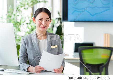 A young business woman operating a computer by the window of a bright office 70319289