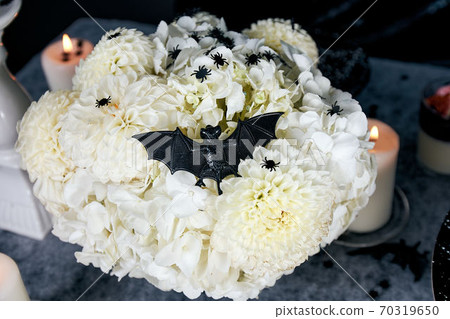 A bouquet of white chrysanthemums and hydrangeas, decorated with a black bat and confetti in the form of black spiders. Halloween holiday concept A bouquet of white chrysanthemums and hydrangeas, decorated with a black bat and confetti in the form of black spiders. Halloween holiday concept 70319650