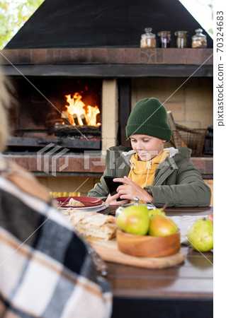 Adorable schoolboy in warm casualwear sitting by table served for outdoor dinner Adorable schoolboy in warm casualwear sitting by table served for outdoor dinner 70324683