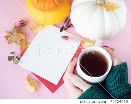Hands holding cup of tea near white paper on red envelope with autumn leaves and pumpkins around Hands holding cup of tea near white paper on red envelope with autumn leaves and pumpkins around 70324689
